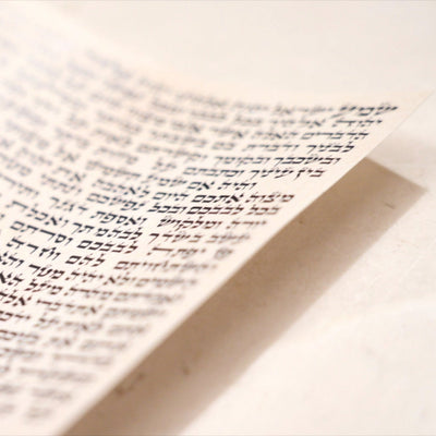 תקריב של טקסט כתוב בכתב סת"ם על קלף מזוזה, מוצג בזווית חדה.